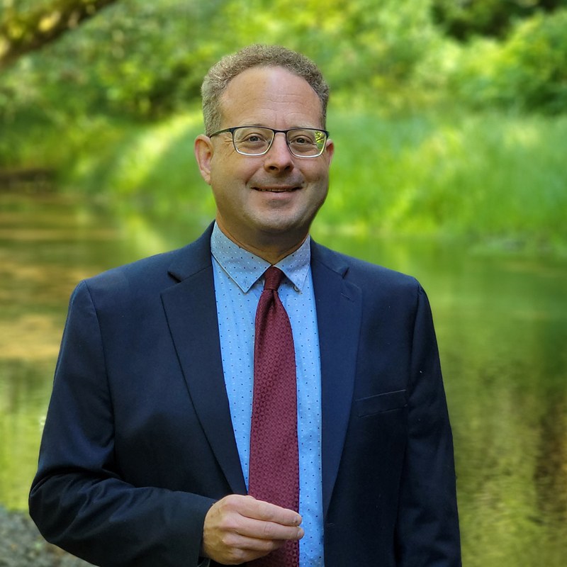 Matt Fadich, founder of inSpark, in a suit beside a river in the Pacific Northwest